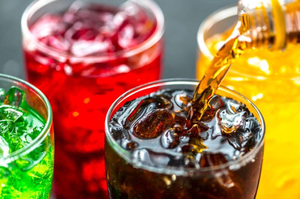 Picture of a fruit flavored sodas in a glass. Dangers of drinking soda.